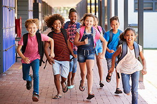 A group of smiling students wearing backpacks runs down an outdoor school hallway